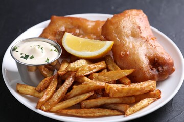 Tasty fish, chips, lemon and sauce on black table, closeup