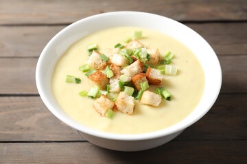 Tasty potato soup with croutons and green onion in bowl on wooden table