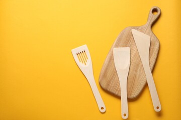 Different wooden spatulas and board on orange background, flat lay. Space for text