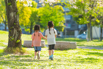 芝生の公園を手を繋いで歩く姉妹