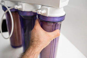 Man hand opens the reverse osmosis system for water purification at home.  - obrazy, fototapety, plakaty
