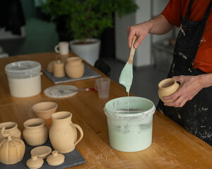 Close-up of a potter's hands glazing a pottery piece. 