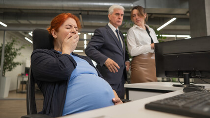 Pregnant woman yawns at work. Colleagues look disapprovingly.  - obrazy, fototapety, plakaty
