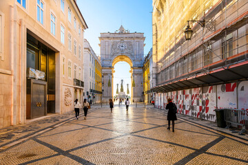 Pedestrians walk on the decorated Portuguese Pavement calçada near the historic Arco da Rua Agusta...
