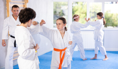 Girl and boy in kimono sparring together in gym during karate training