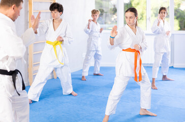 Fototapeta na wymiar Group of preteen children in kimono trying new martial moves at karate class