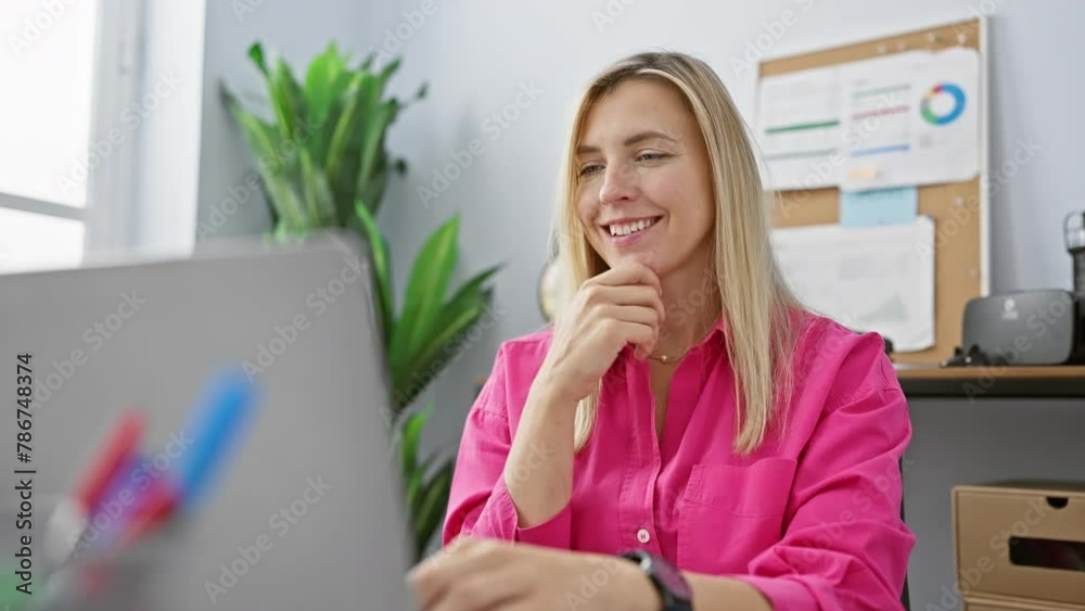 Sticker Smiling young woman working on a laptop in a modern office setting, dressed in a bright pink shirt.