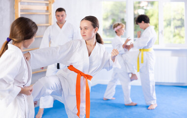 Fototapeta na wymiar Two girls in kimonos practice karate techniques in group at gym
