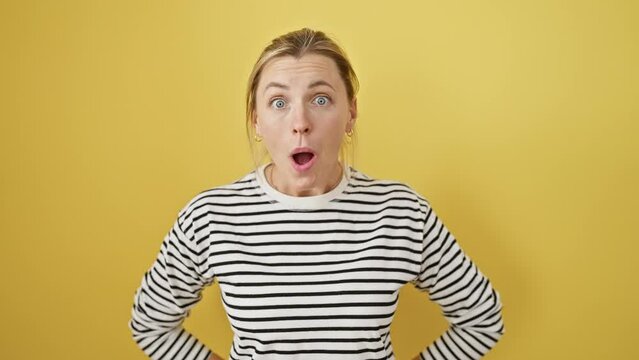 Astonished young blonde woman standing, expression of shock and fear on her face. overcome with amazement, excited surprise. isolated on yellow background.