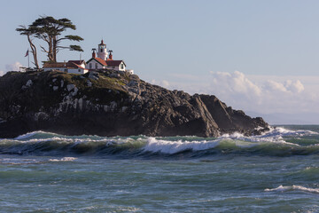 A lighthouse sits on a rocky hillside. The lighthouse is white and red, and it is surrounded by a...