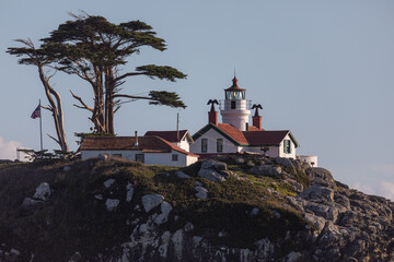 A lighthouse sits on a rocky hillside. The lighthouse is white and red, and it is surrounded by a lush green hillside. The scene is peaceful and serene. Battery Point Lighthouse, California. - 786752781