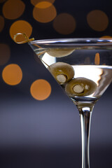 A martini glass with olives in it. The olives are marinating inside of the drink and the glass is full