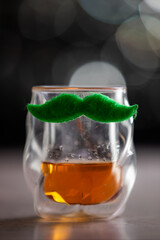 A glass with a mustache on it. The glass is filled with whiskey. The mustache adds a playful and whimsical touch to the glass for St Patrick's day.