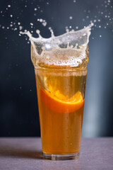 A glass of beer with an orange slice in it splashing out of the glass