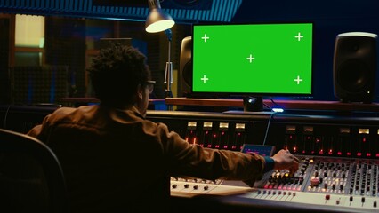 African american audio engineer uses greenscreen on pc in professional recording studio, working...