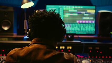 African american tracking engineer processing and mixing sounds in control room, operating audio console with moving faders and colored meters. Technician producer deals with technical gear. Camera B.