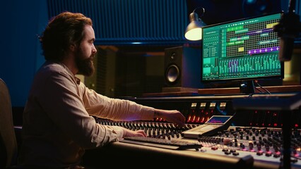 Professional tracking engineer editing music by adding sound effects in control room at studio, recording tracks and using mixing console. Producer operates technical equipment. Camera B.