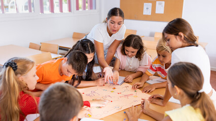 Female teacher and pupils playing board game together in classroom.