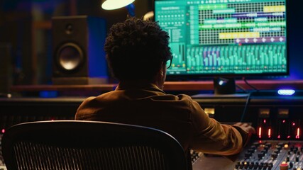 African american music producer mixing and mastering tracks on audio console, twisting knobs and...