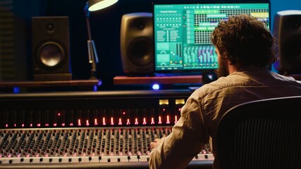 Sound engineer recording and editing tracks in control room, working with mixing console and...
