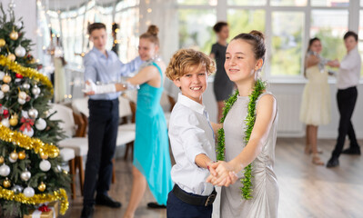 Naklejka premium Couple of smiling teenagers, boy and girl in festive clothing performing graceful waltz with group of peers under guidance of female teacher during Christmas event in college
