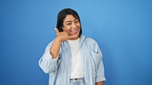 Hispanic middle-aged woman making call-me gesture against blue wall