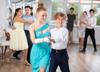 With unhurried music, teen boy and girl in couple spins to rhythm of tango during lesson for novice students. Classes in mini-groups for those who want to learn dancing