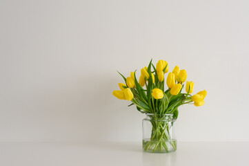 A vibrant arrangement of yellow tulips in a glass vase against a pristine white backdrop. Ample...