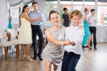 Positive teen boy and girl are dancing contemporary modern discofox in couple during lesson at...