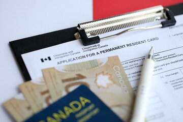 Application for permanent resident card on table with pen and canadian passport with money close up
