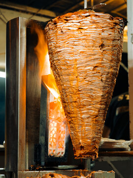 Vertical image Grilling traditional trompo al pastor street taco pork meat on spit with flames at night in Mexico.