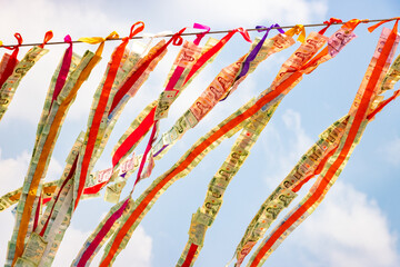 Thai banknotes attached to a rope flutter in the wind against the sky, Thailand