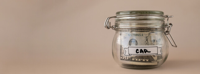 Saving Money In Glass Jar filled with Dollars banknotes. CAR transcription in front of jar....