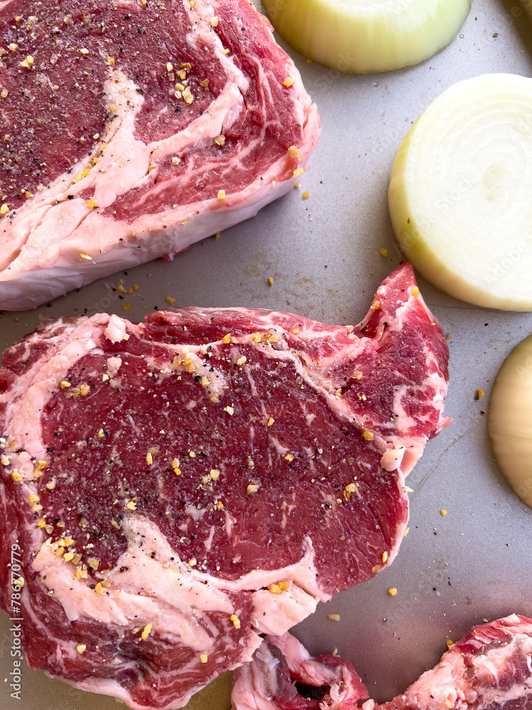 Wall mural raw ribeye steaks seasoned with spices and onion halves on tray