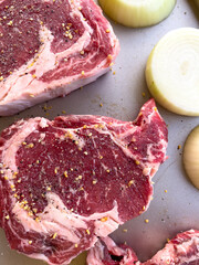 Raw Ribeye Steaks Seasoned with Spices and Onion Halves on Tray - 786770779