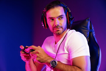 Smart gaming streamer concentrating gaming players trying to pass the level at mission completed with joystick control, talking others via mic on streaming live at neon lighting studio room. Surmise.