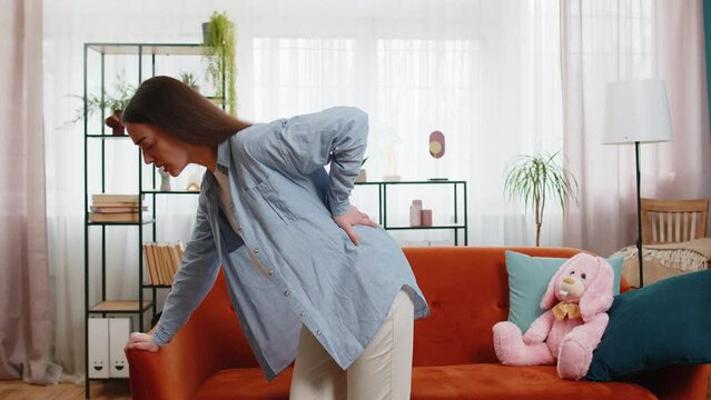 Upset young pregnant woman lady suffering from lower back pain sitting on sofa couch in living room at home. Illness future parent female on couch and feeling sick touching big belly in apartment.