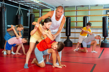Young boys and girls in pairs training armlock move on each other in gym.