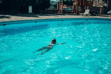 A woman is swimming in a pool. The water is clear and calm. The woman is wearing a black swimsuit.