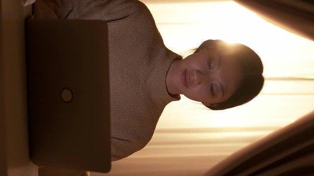 Vertical video. Home learning. Online education. Smart woman watching virtual class using laptop taking notes sitting room workplace interior.