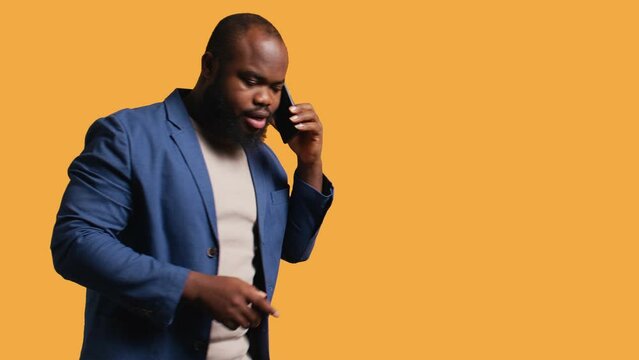 African american man enjoying talking with friends phone call using smartphone, studio background. BIPOC person walking around conversating during telephone call, camera B
