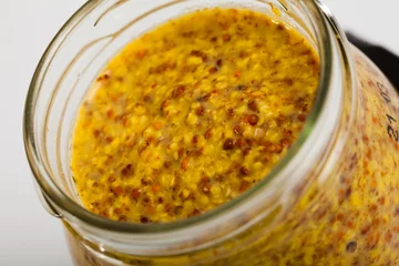 Poster Closeup of soft and mild grainy mustard in open glass jar on white surface. Organic condiment © JackF