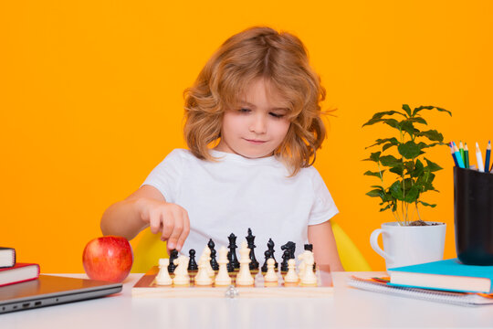 Little kid play chess. Thinking child. Chess game for kids. Intelligent, smart and clever school boy. Kid with chess on yellow isolated studio background.