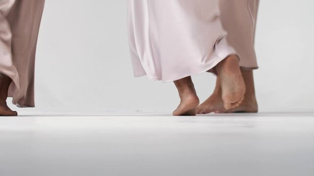 Close-up of the beautiful legs and feet of three young women running barefoot away from the camera, dressed in beautiful beige gowns. Close up. Slow motion. 4k