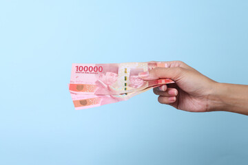 Woman hand showing rupiah Indonesian money on blue background