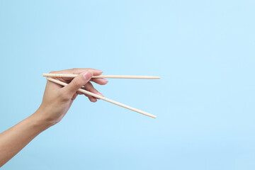 Hand using bamboo chopsticks against blue background