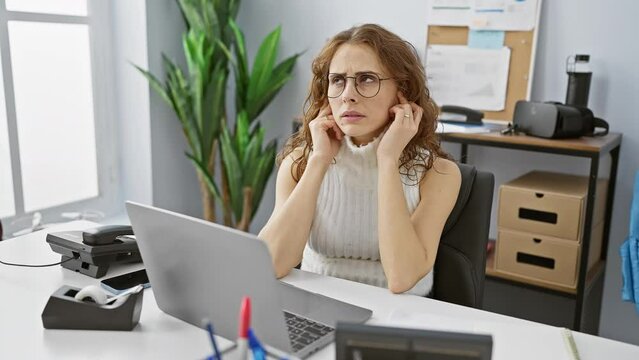 Beautiful young office worker annoyed by loud noise, covering ears with fingers. indoor portrait showing headache, stress at the workplace, deaf to the din!