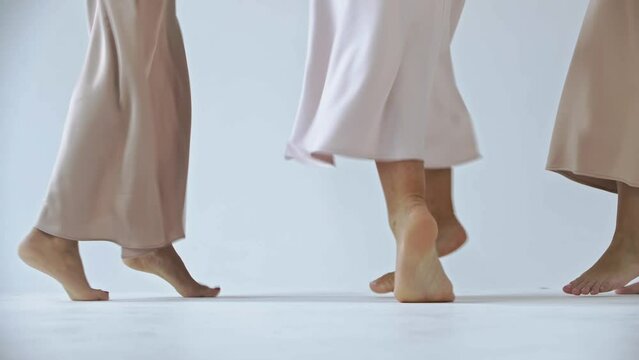 Three pairs of female feet dance barefoot on a snow-white cyclorama backdrop in the studio. Close up. Slow motion. 4k
