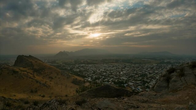 Timelapse of clouds over the Osh city. Skyline panoramic view at sunset over rooftops in small city in afternoon, golden hour time. View of Osh city  from the Sulaiman Too mountain, Kyrgyzstan. 