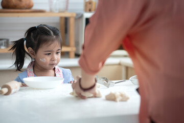 Little girl was playing with the bread dough that was placed on the table, she looked and wanted to try making bread like her mother, selective focus - obrazy, fototapety, plakaty